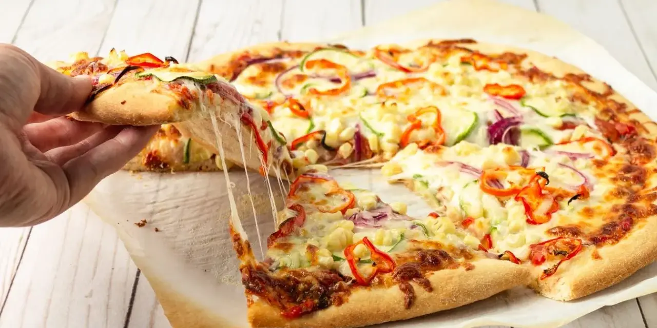 Pyszna pizza domowa z ciągnącym serem, papryką, cebulą i cukinią. Ktoś właśnie podnosi kawałek.
