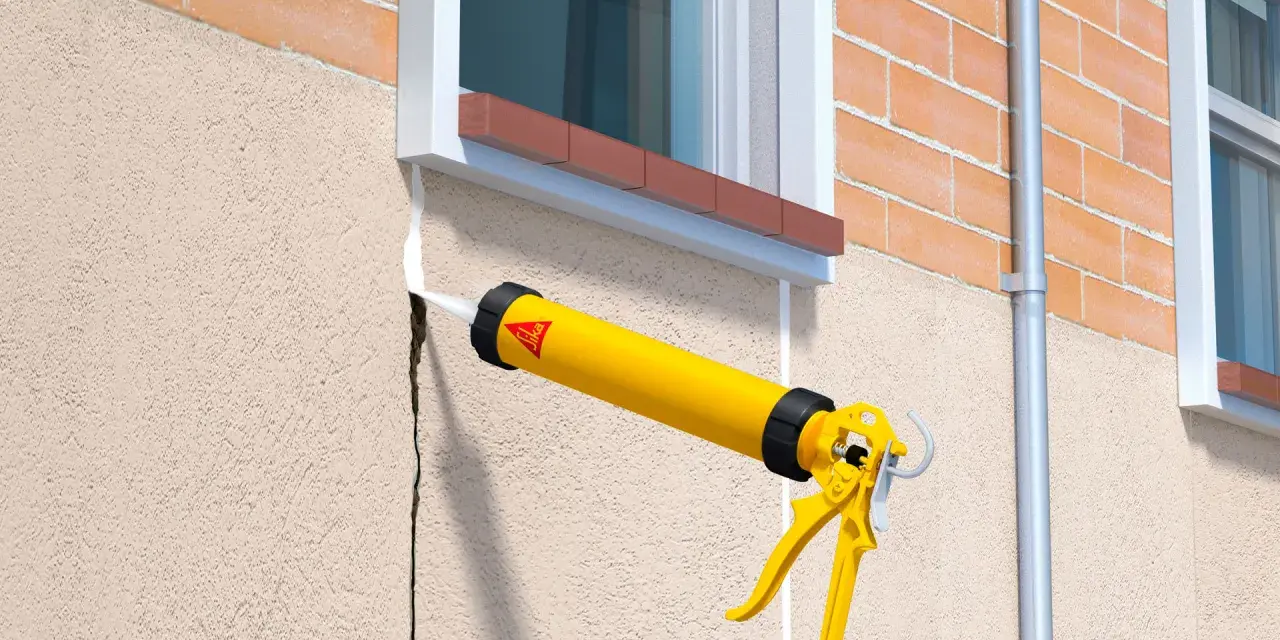 Pistola aplica sellador blanco en una grieta del rebozado de la pared exterior, junto a una ventana.