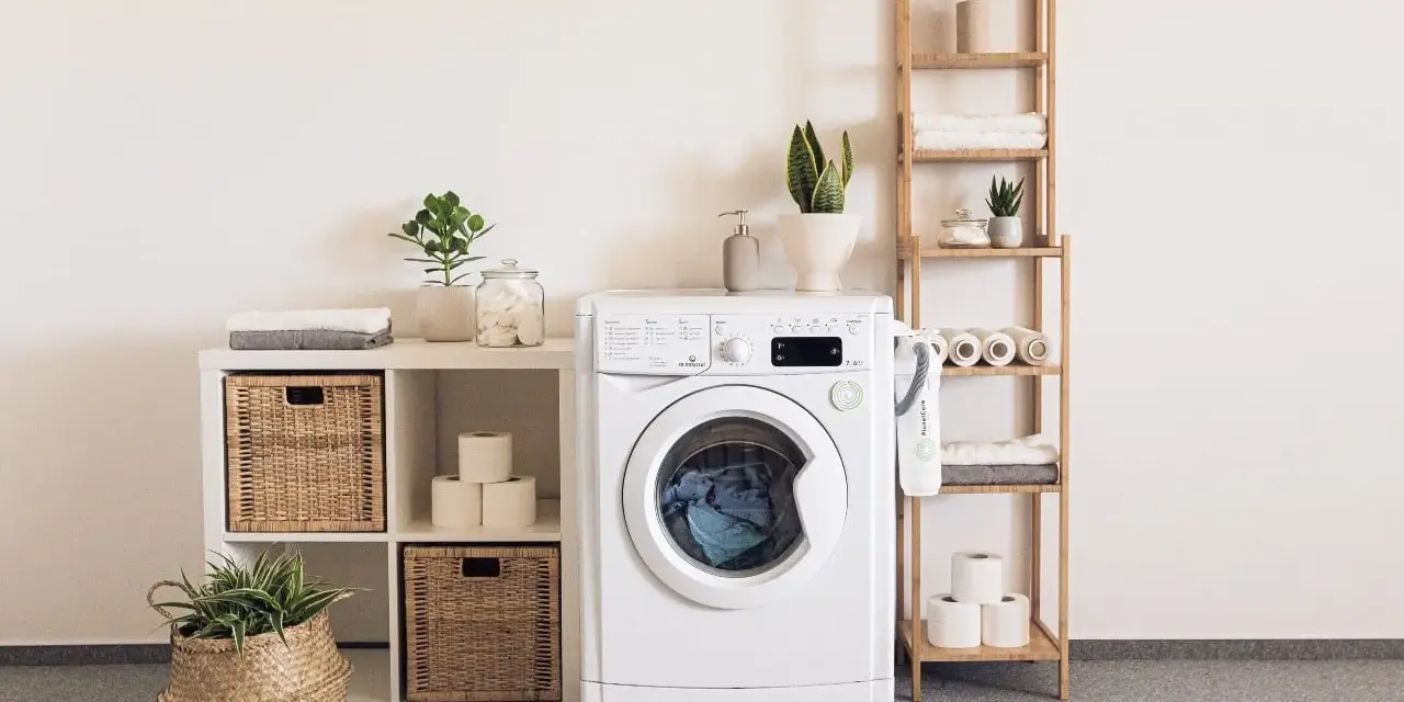 Lavadora blanca con cesta de mimbre, plantas y accesorios que se colocan en una prenda.