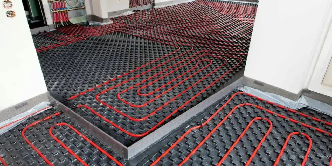 Instalación de un sistema de calefacción por suelo radiante, con tuberías rojas serpenteando sobre una base negra. Preparando un suelo refrescante para el confort.