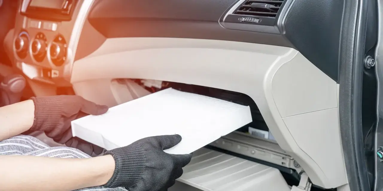 Wymiana filtra kabinowego w Audi A3 8L. Ręce w rękawiczkach wyjmują biały filtr z wnętrza schowka.