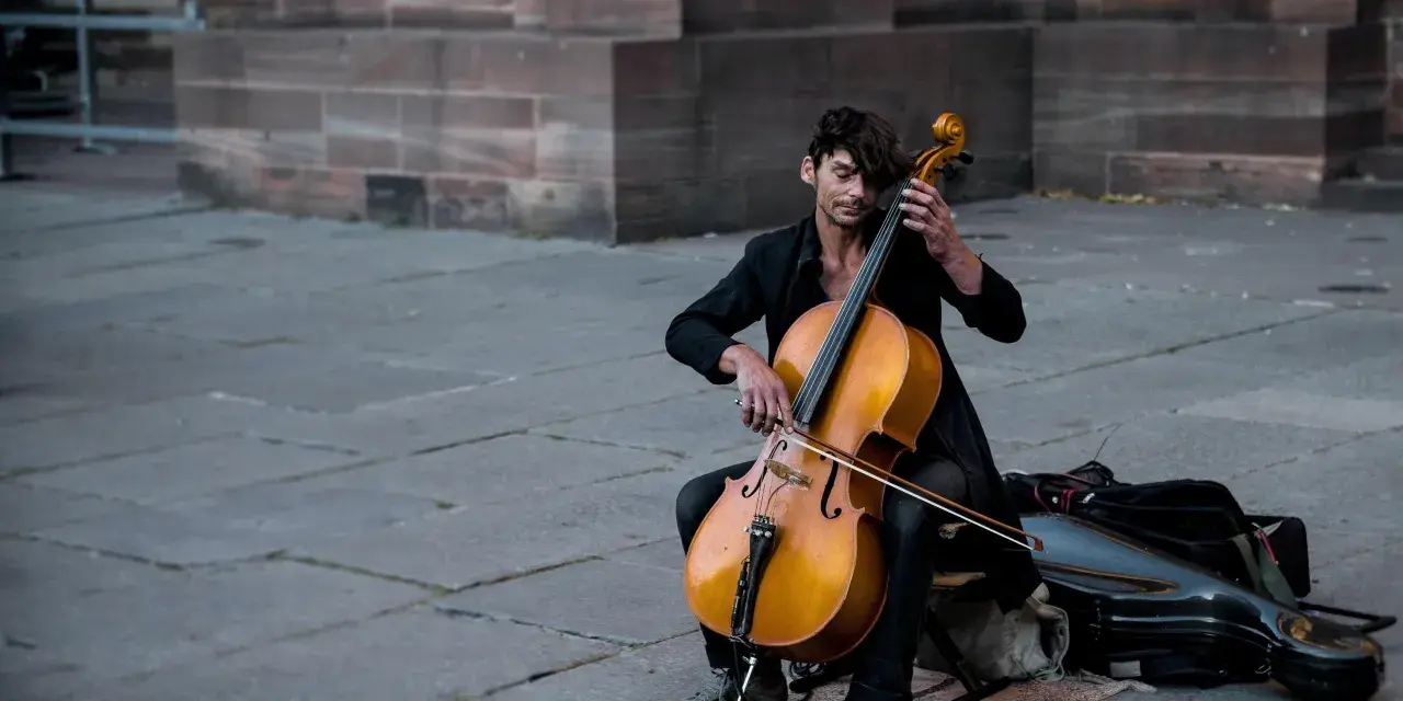 Ein Mann spielt auf einem Cello-Musikinstrument vor einer Steinfassade.