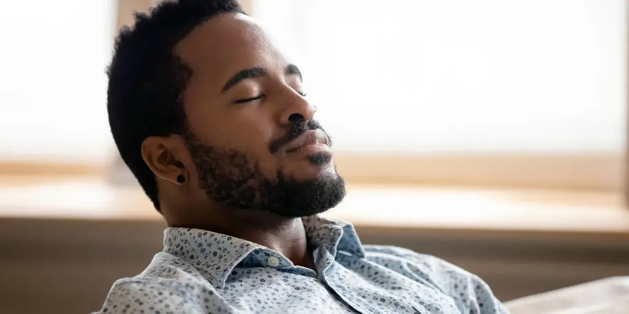 A man with closed eyes and a beard breathes deeply, finding a moment to ground himself amidst the day's chaos.
