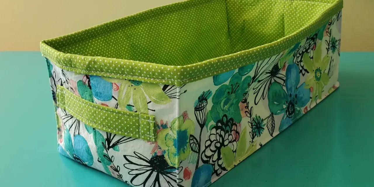 Panier rectangulaire en tissu, doublé de pois verts. Son extérieur est orné d'un motif floral coloré, parfait pour ranger vos affaires avec style.