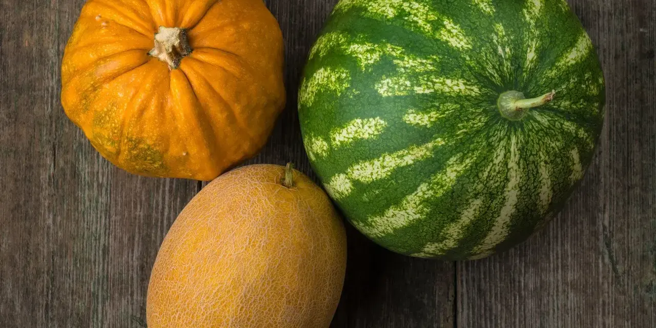 Dynia, melon i arbuz leżą na drewnianym blacie.