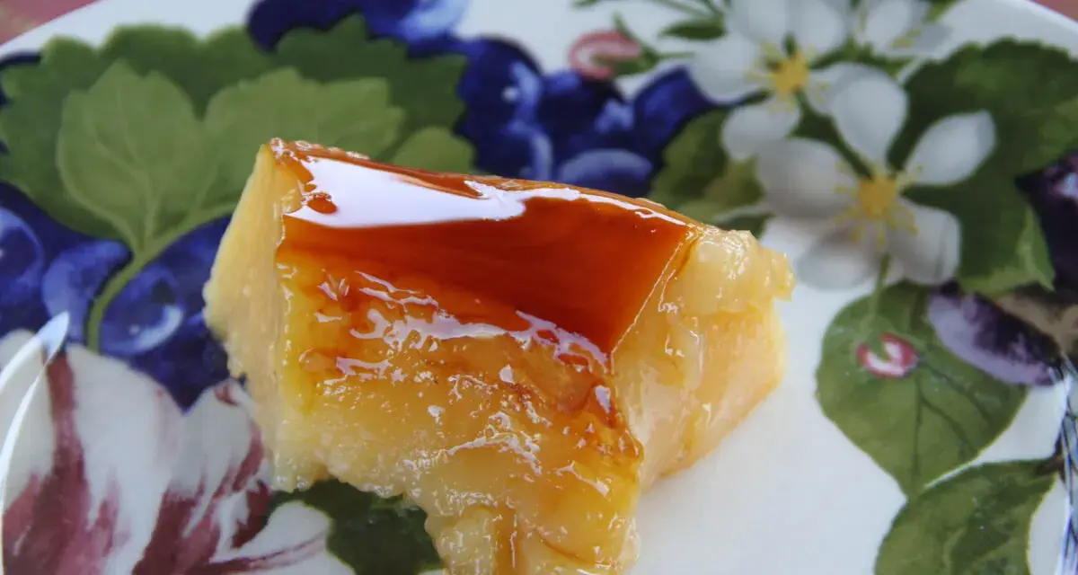 Un trozo de tocino de cielo de la abuela, con su caramelo brillante, sobre un plato decorado con flores y frutos.