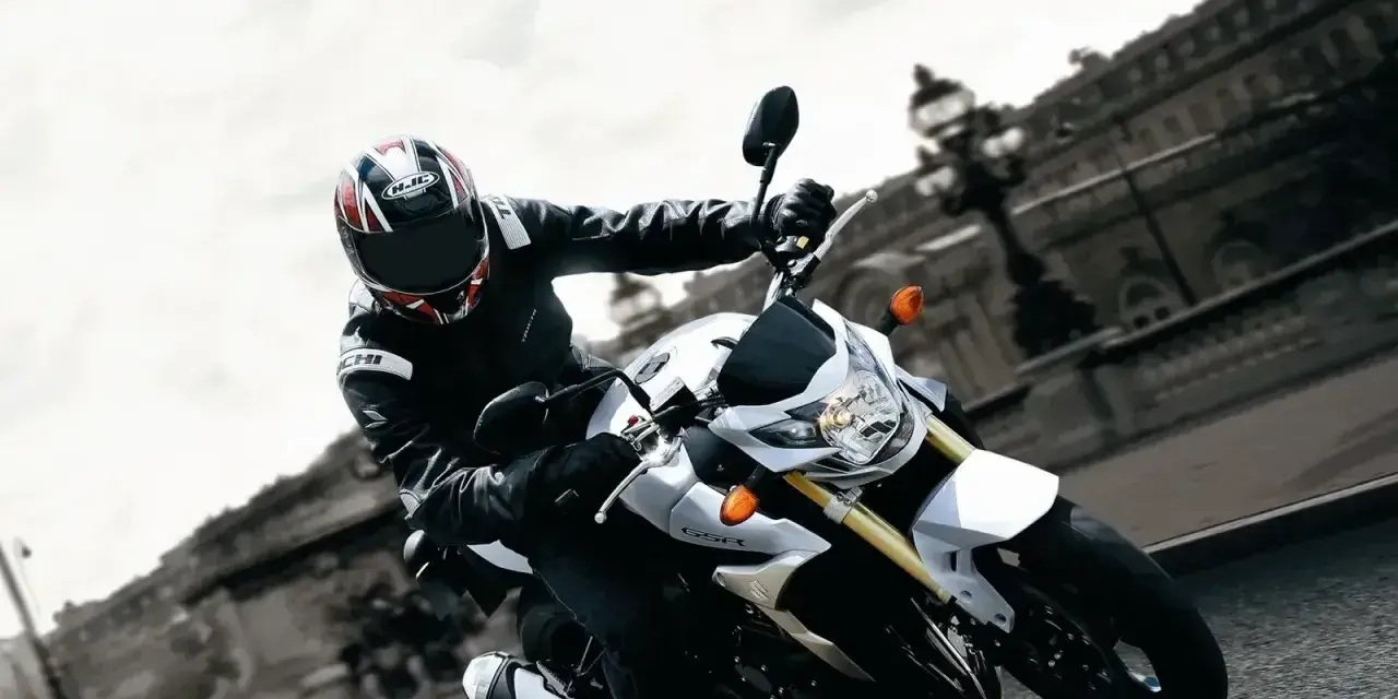 Motocyklista na białym Suzuki GSR 750 pokonuje zakręt. Nawet z potencjalnymi wadami, jazda nim to czysta przyjemność.