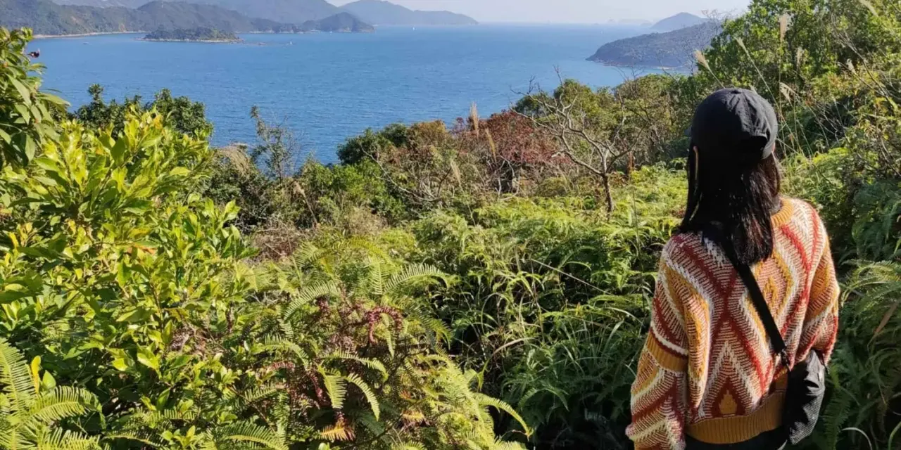 Frauen genießen die Aussicht beim Hong Kong Hiking. Grüne Vegetation und das blaue Meer erstrecken sich bis zu den Hügeln.
