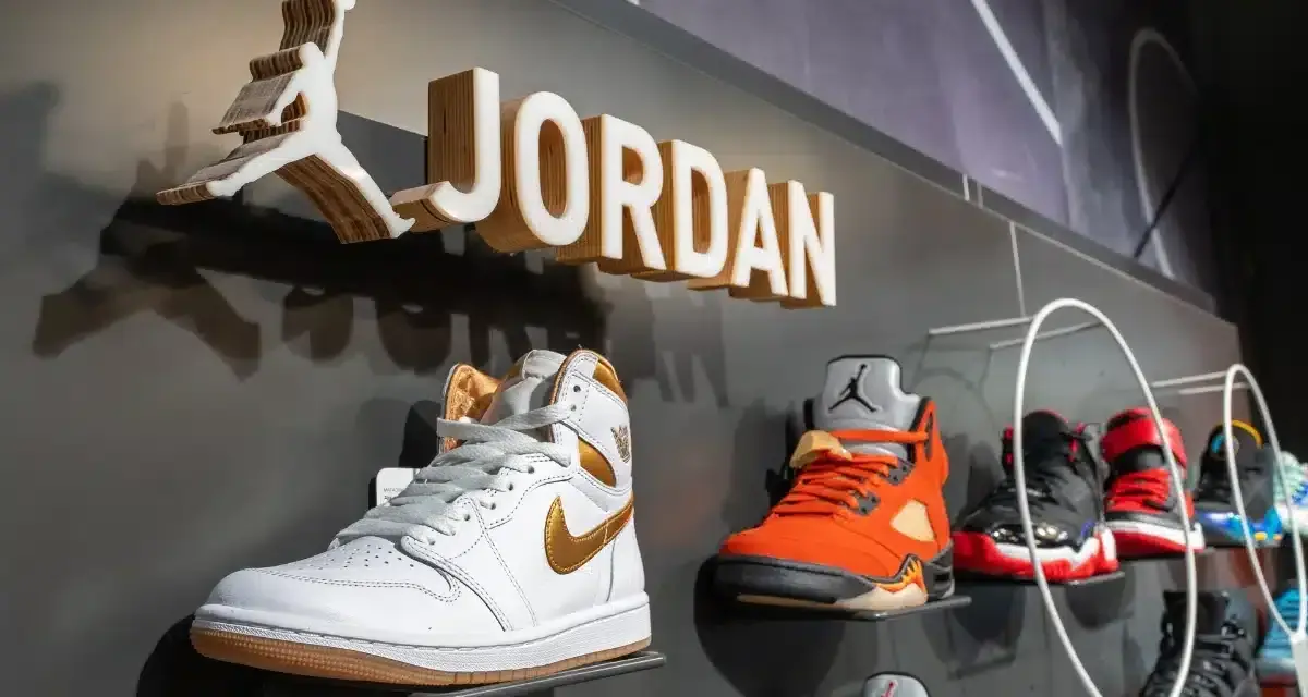 Na wystawie butów Jordan, białe Air Jordan 1 z złotymi akcentami. Obok pomarańczowe Air Jordan 5. Czy 8 5 jaki to rozmiar buta?