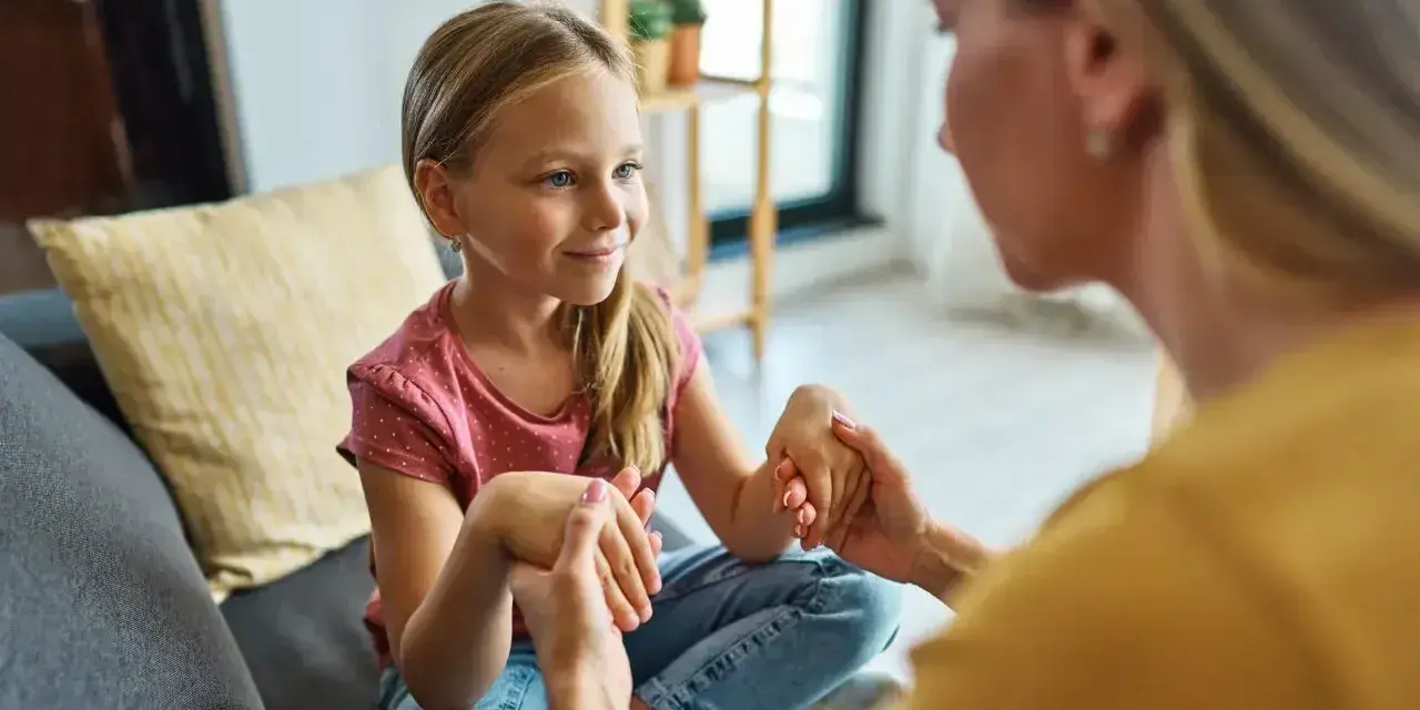 Mama spokojnie tłumaczy córce, jak rozmawiać z dzieckiem o złym zachowaniu. Dziecko słucha uważnie, trzymając dłonie mamy.
