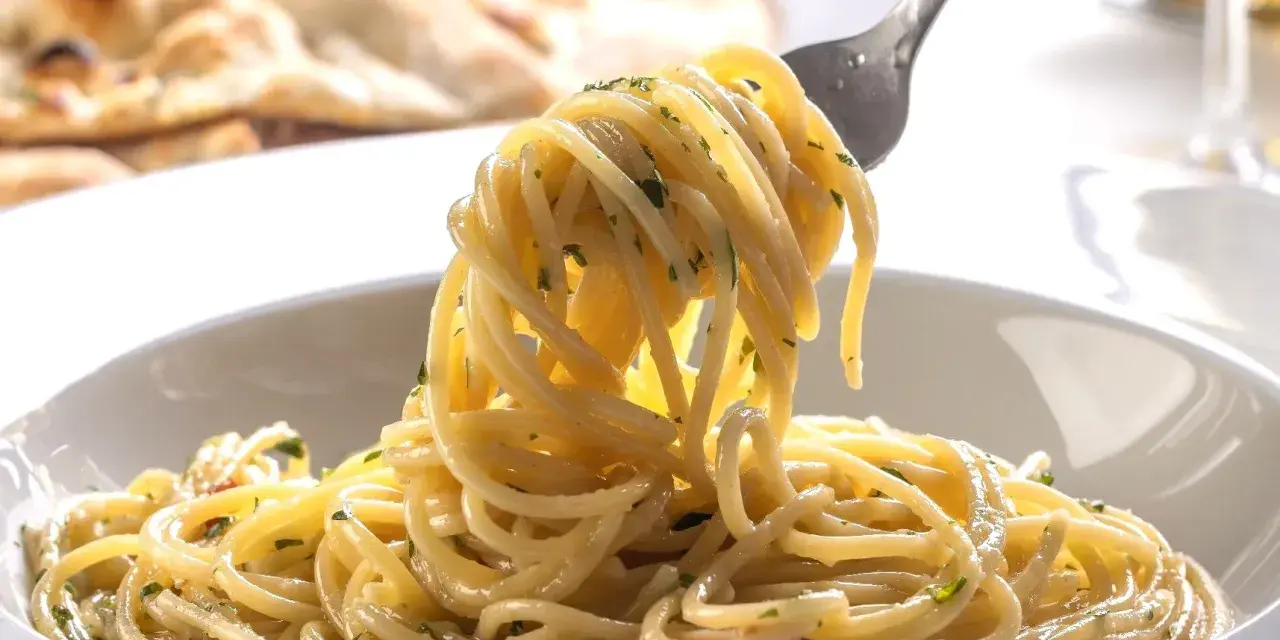 Porcja spaghetti z ziołami na widelcu, w tle płaski chleb.