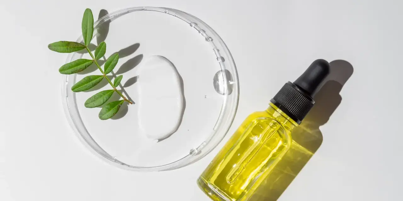 Kropla białego kremu i żółte serum w buteleczce z pipetką, obok gałązka z liśćmi. Składniki do walki z trądzikiem, w tym retinoidy na trądzik.