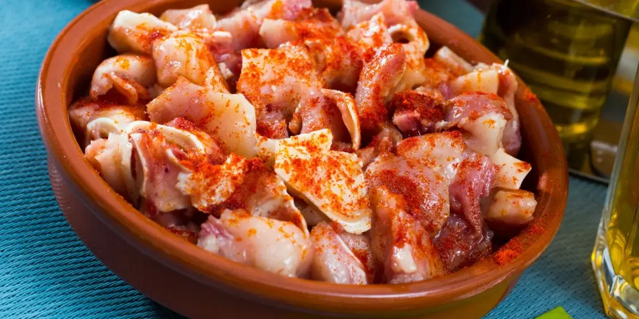 Oreja a la gallega, trozos de oreja de cerdo con pimentón en una cazuela de barro, listos para disfrutar.