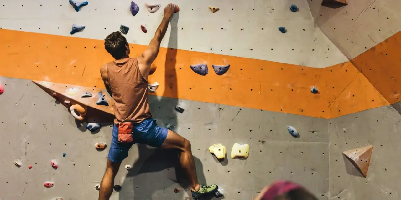 Mężczyzna wspina się po ścianie z kolorowymi chwytami. To właśnie bouldering – wspinaczka bez liny na niskich ściankach.
