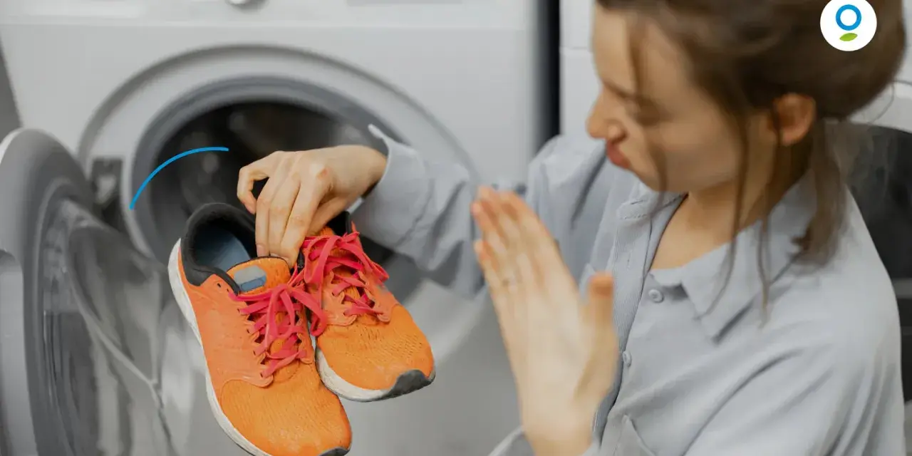 Woman holding smelly orange sneakers near an open washing machine.