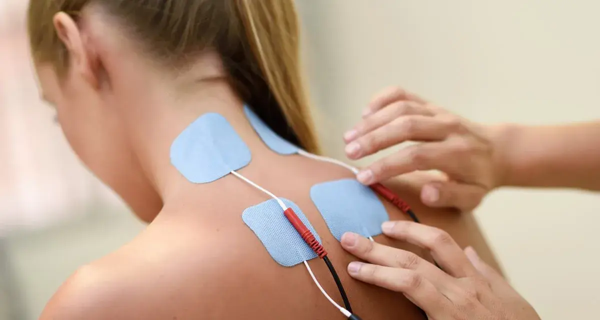 Elektrody na plecach kobiety podczas terapii fizykalnej. Terapeuta przygotowuje do zabiegu.