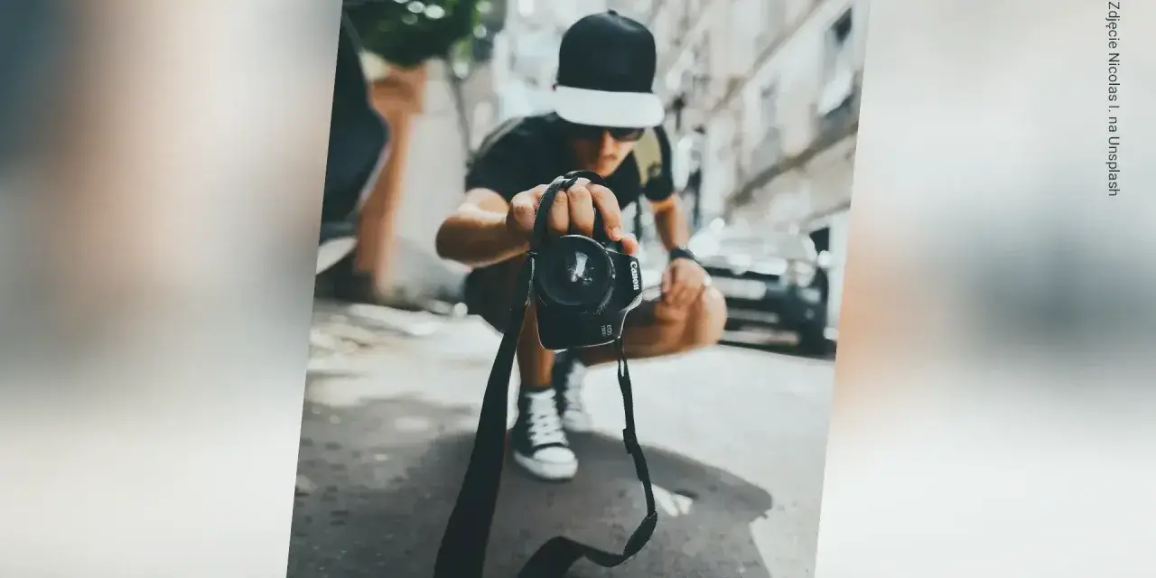 Młody fotograf w czapce z daszkiem trzyma aparat, zastanawiając się, ile zarabia fotograf w dzisiejszych czasach.