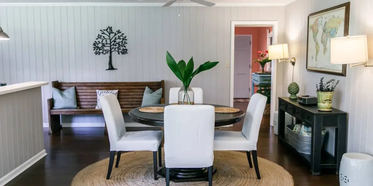 Elegante decoracion comedor pequeño con mesa redonda, sillas blancas, banco de madera y arte de árbol en la pared.