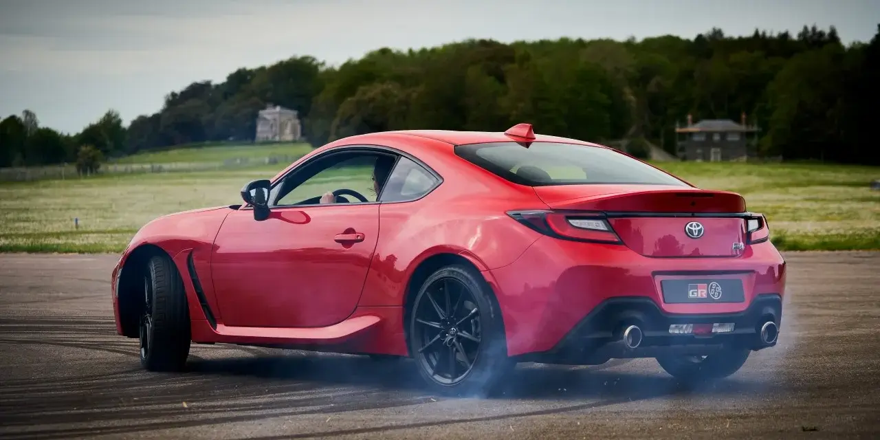 Czerwona Toyota 86 GR w poślizgu, z opon dymiących na asfalcie. W tle zielone pola i drzewa.