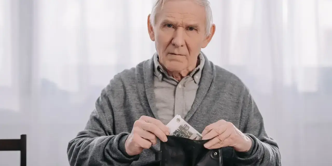 Zmartwiony starszy mężczyzna wkłada pieniądze do portfela, planując wcześniejszą emeryturę.