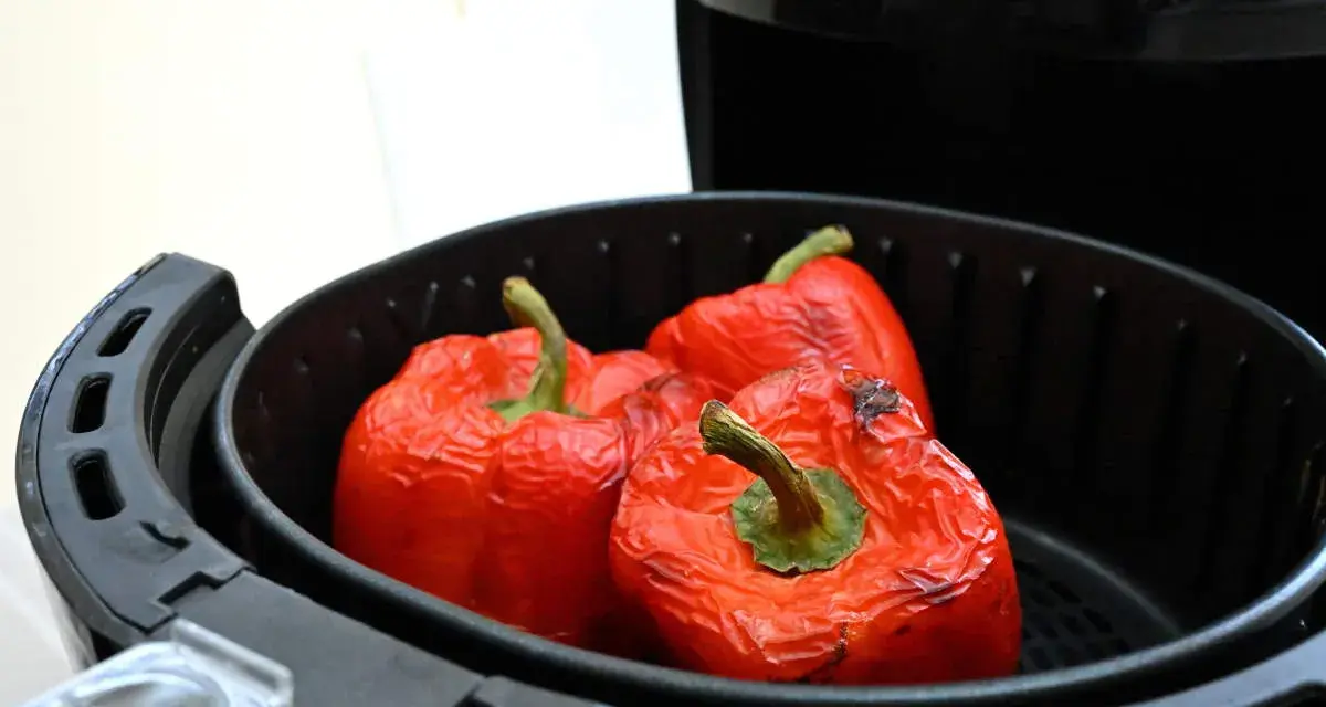 Tre peperoni rossi interi, leggermente abbrustoliti, pronti per essere cucinati nella friggitrice ad aria.
