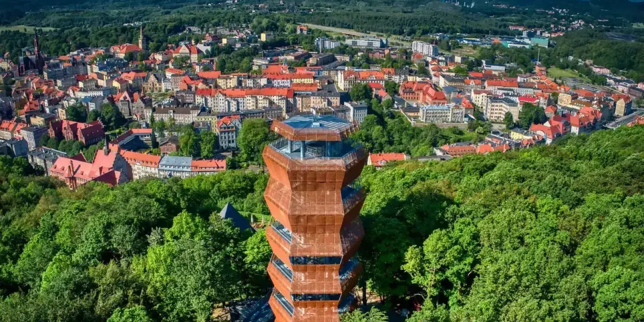 Nowoczesna wieża widokowa w otoczeniu zieleni, z panoramą miasta Wałbrzych i Sudetów Wałbrzyskich w tle.