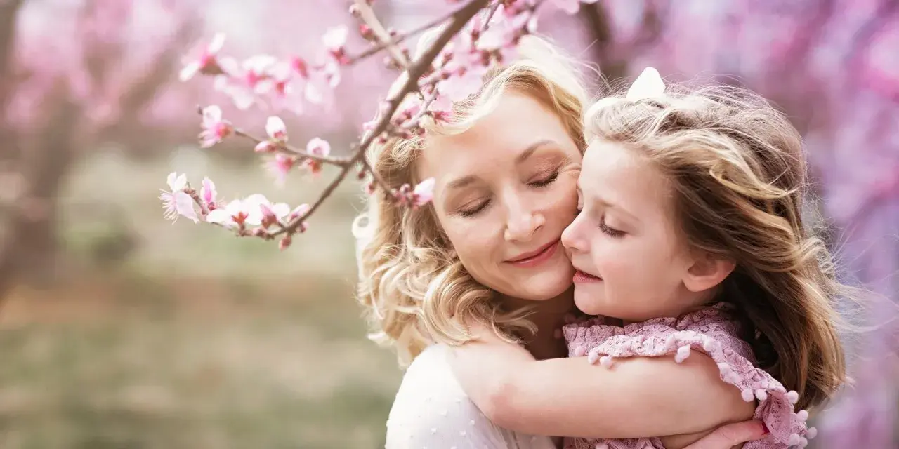 Córka tuli mamę pod kwitnącą wiśnią. Idealny obraz na Dzień Mamy.