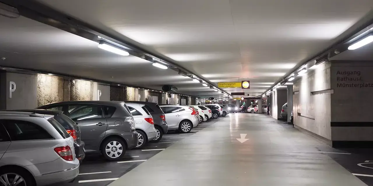Podziemny parking z rzędami samochodów. Dostępny jest wynajem miejsca parkingowego.