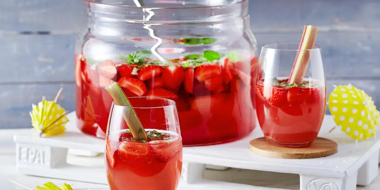 Erfrischende Rhabarber Bowle mit Erdbeeren und Minze, garniert mit Rhabarberstücken. Perfekt für den Sommer!