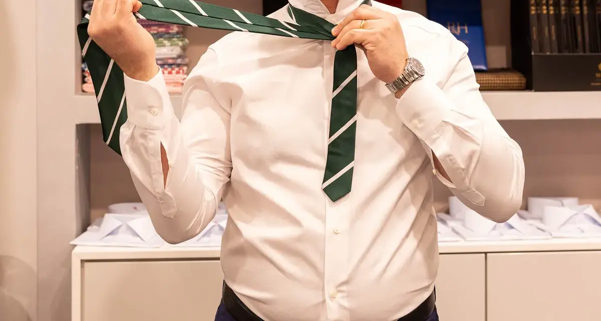 Uomo in camicia bianca che impara come fare il nodo alla cravatta verde a righe.