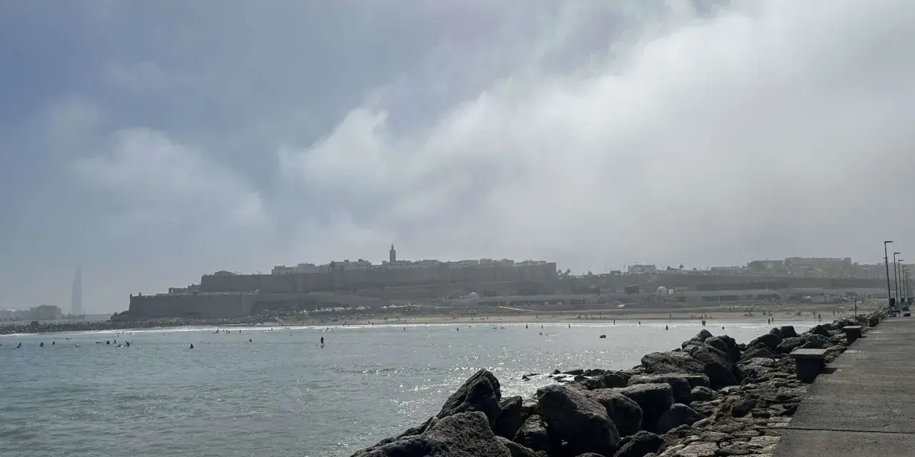 Spokojna plaża z surferami i miastem w tle. Czy Maroko jest bezpiecznym krajem? Widok sugeruje, że tak, ludzie cieszą się słońcem i morzem.