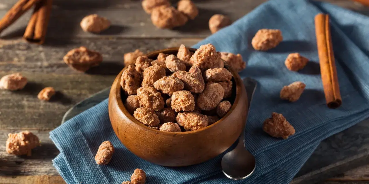 Schüssel mit gebrannten Mandeln, Zimtstangen und Löffel. Ein süßer Snack, der auch in der Schwangerschaft genossen werden kann.