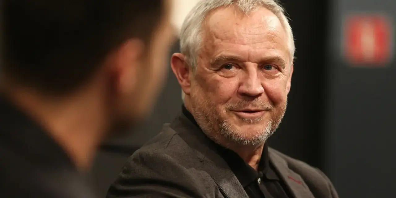 Uśmiechnięty Mikołaj Kondrat w szarym garniturze, rozmawiający z kimś niewidocznym na pierwszym planie.
