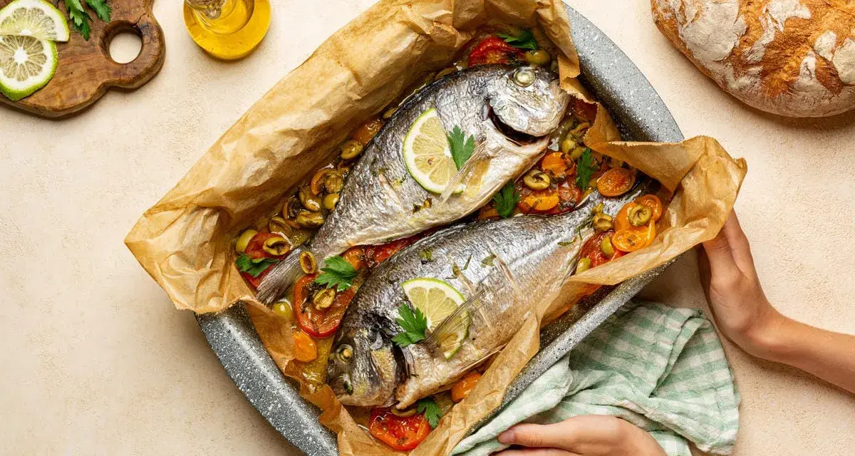Due agoni in carpione cotti al forno con pomodorini, olive e limone, pronti per essere gustati.
