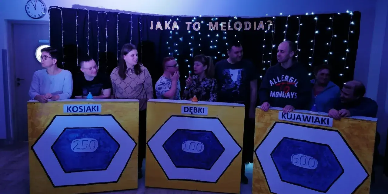 Uczestnicy zabawy "Jaka to melodia?" stoją przy planszach z nazwami drużyn: Kosiaki, Dębki, Kujawiaki.