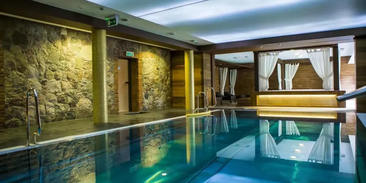Basen w spa na Kaszubach. Kamienne ściany, turkusowa woda i zaciszne altany z białymi zasłonami tworzą atmosferę relaksu.