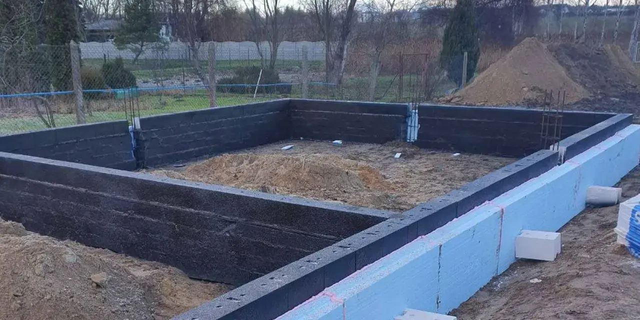 Budowa domu w toku: wylewane fundamenty z izolacją, widoczne zbrojenie i piasek.