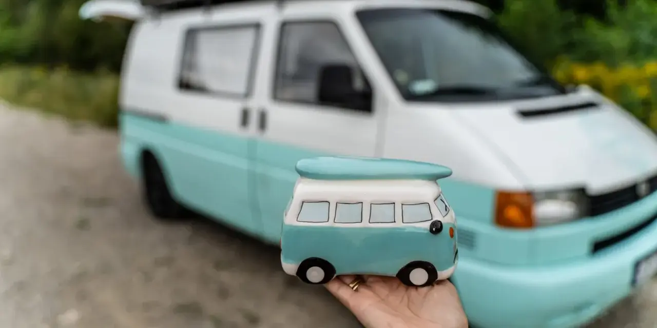 Mała figurka t4 camper w ręce, na tle prawdziwego, turkusowo-białego kampera.