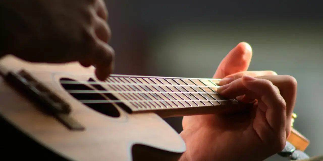 Dłonie grające na ukulele, zbliżenie na gryf i struny.
