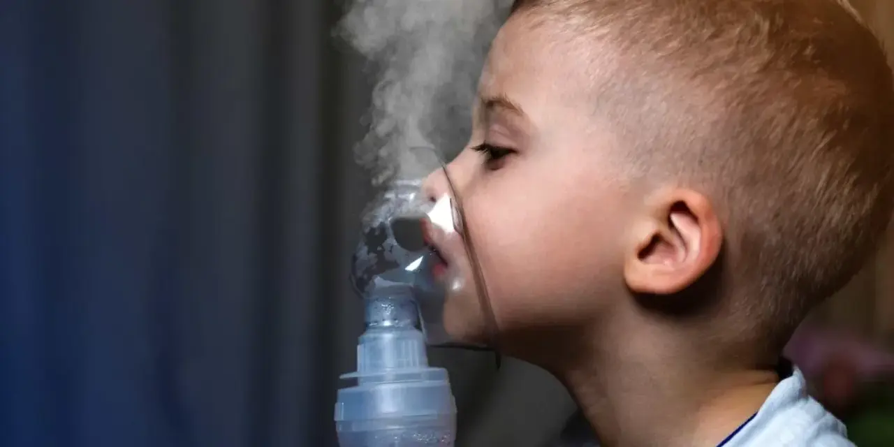 Chłopiec z maską inhalatora na twarzy, wdychający parę.
