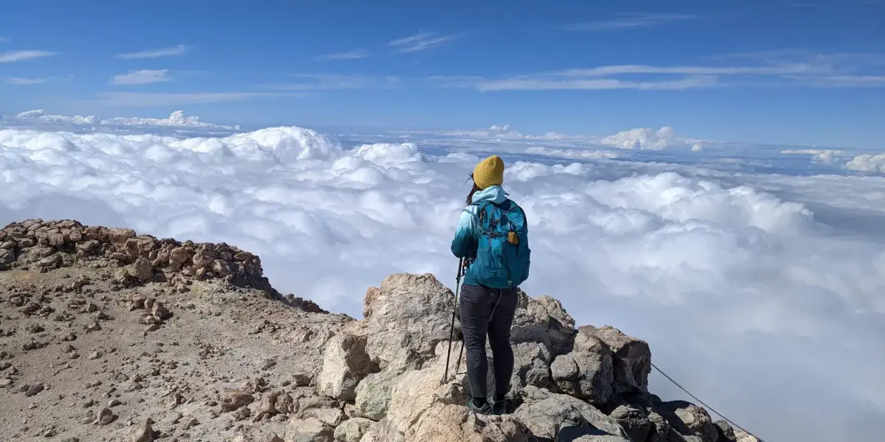 Widok z Teide: turystka w żółtej czapce podziwia morze chmur z wulkanicznego szczytu.