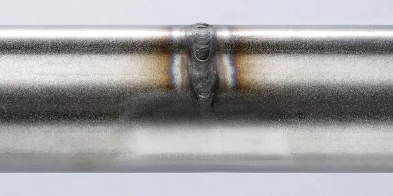 Dettaglio di una saldatura acciaio inox su un tubo metallico, con sfumature iridescenti intorno al cordone.