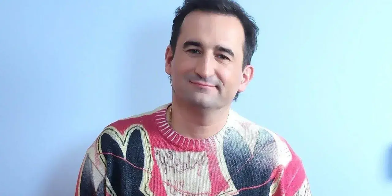 Uśmiechnięty polski aktor z autyzmem w kolorowym swetrze z sercem i napisem "Yo Baby".
