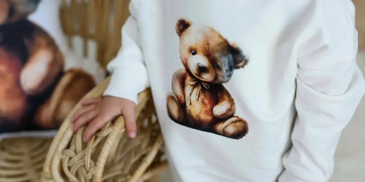 Biała bluza Moschino z uroczym misiem w stylu vintage. Dziecko trzyma się wiklinowego koszyka.