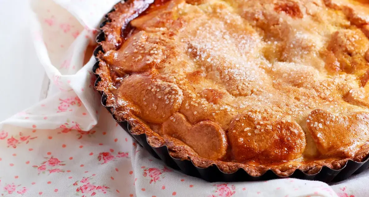 Une délicieuse tarte au sucre dorée, saupoudrée de cristaux de sucre, repose sur une serviette à motifs floraux roses.