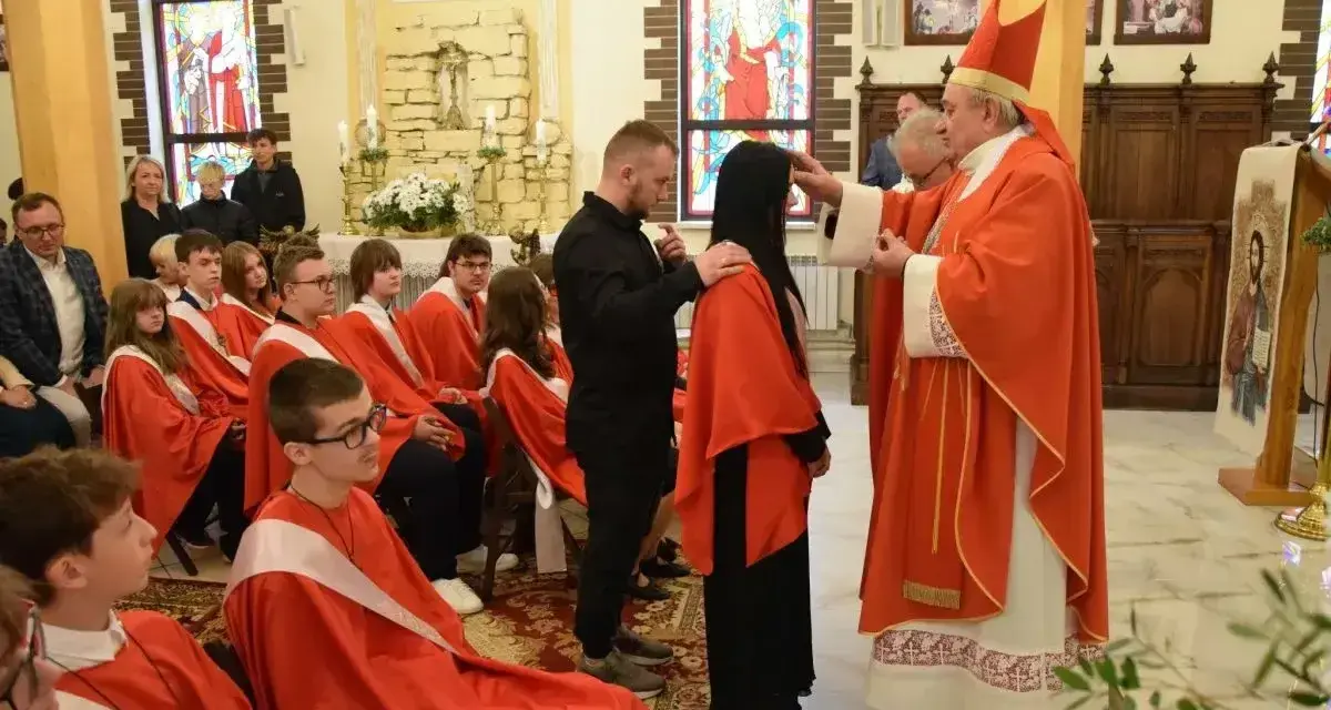 Biskup udziela sakramentu bierzmowania. Ceremonia, choć uroczysta, nie trwa długo. Młodzi ludzie w czerwonych szatach czekają na swoją kolej.
