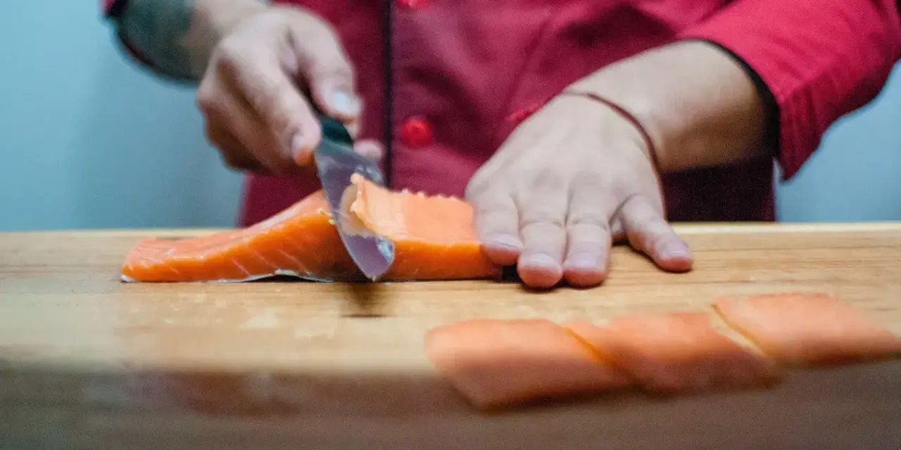Szef kuchni kroi łososia na desce. Powstają kawałki idealne do sushi, które można zamarynować w solance.