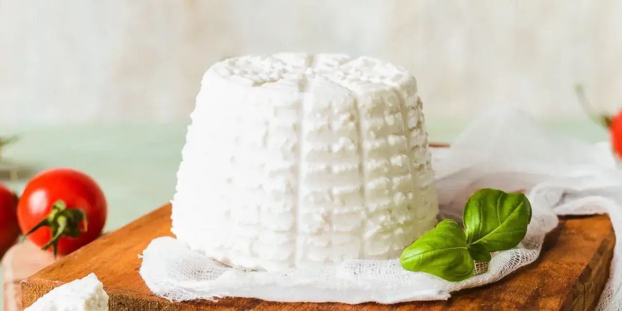 Świeża ricotta na desce, obok pomidorki i bazylia. Niskie ricotta kalorie czynią ją idealną dla dbających o linię.