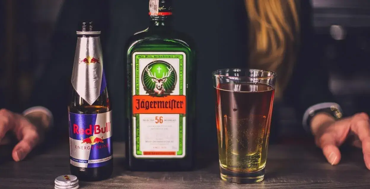 Butelka Jägermeister, puszka Red Bull i szklanka z drinkiem. Jägermeister to niemiecki likier ziołowy, często mieszany z napojami energetycznymi.