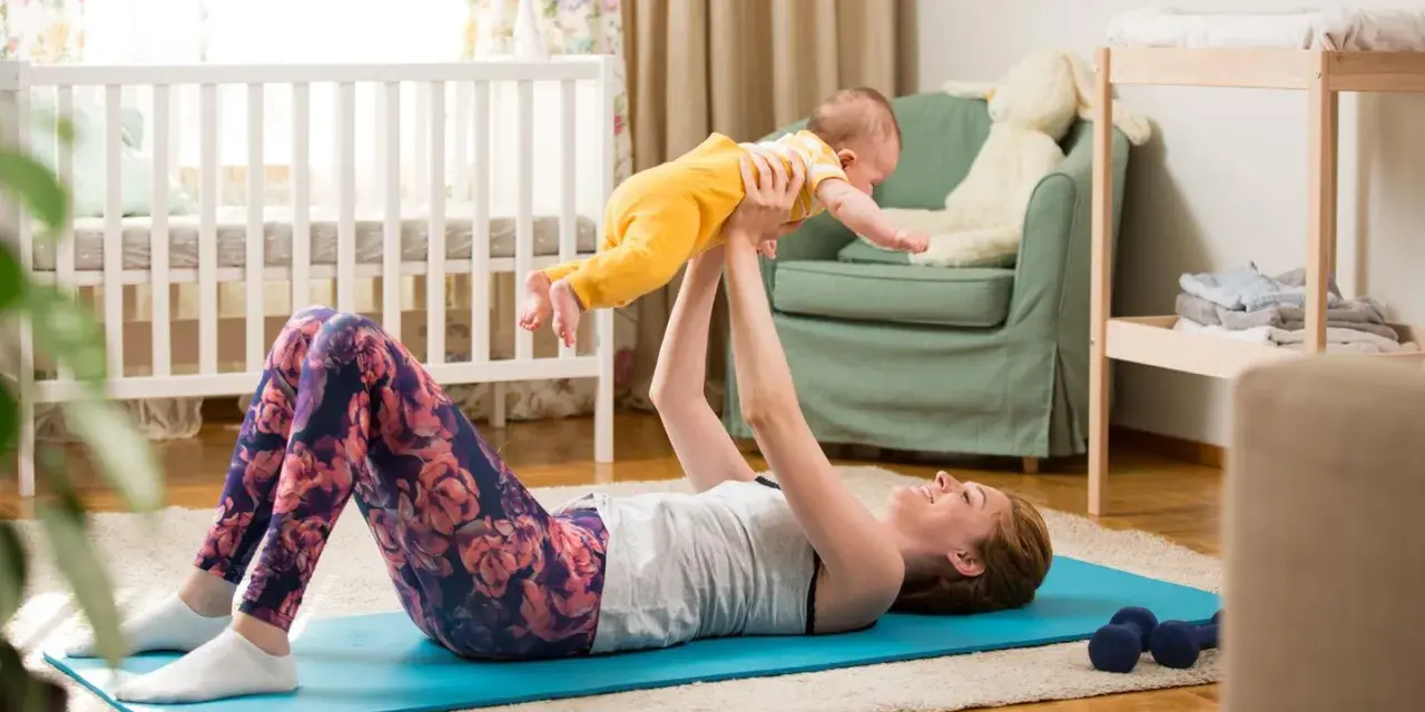 Frau macht Beckenbodentraining mit Baby. Sie liegt auf einer Matte und hebt ihr Kind hoch.